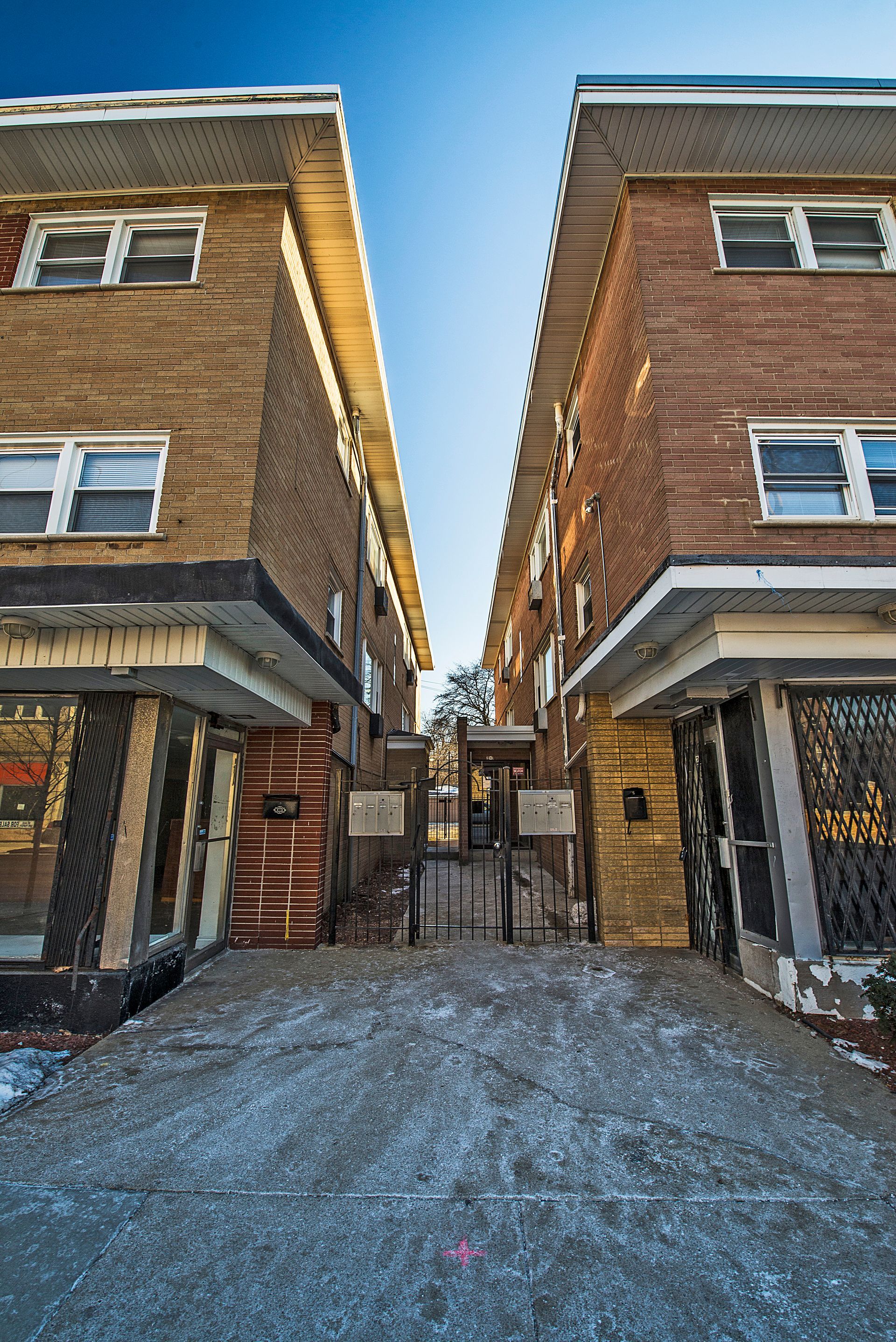 Two brick apartment buildings, a gated alleyway between them.