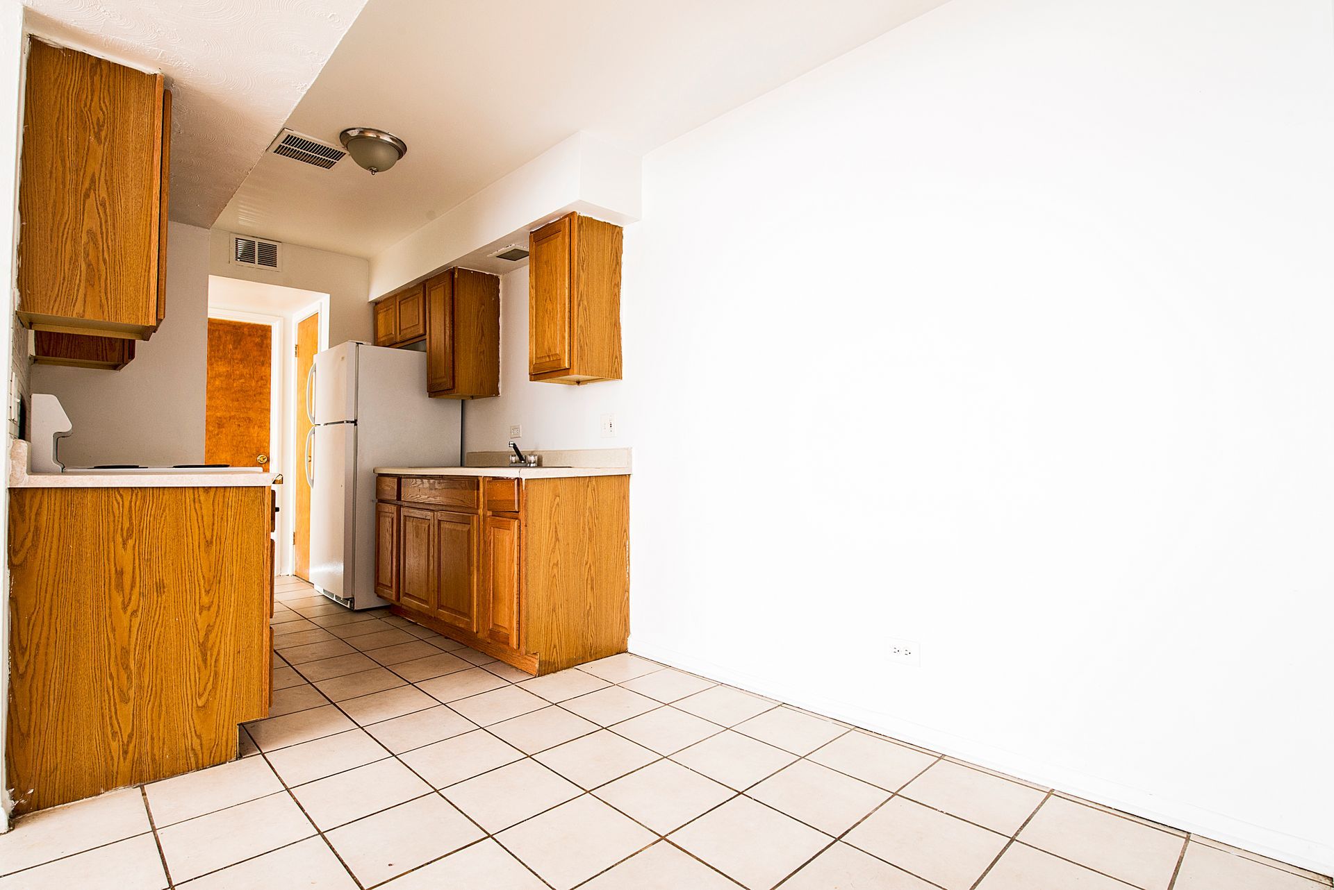 Empty kitchen with wood cabinets, white appliances, and tiled floor.