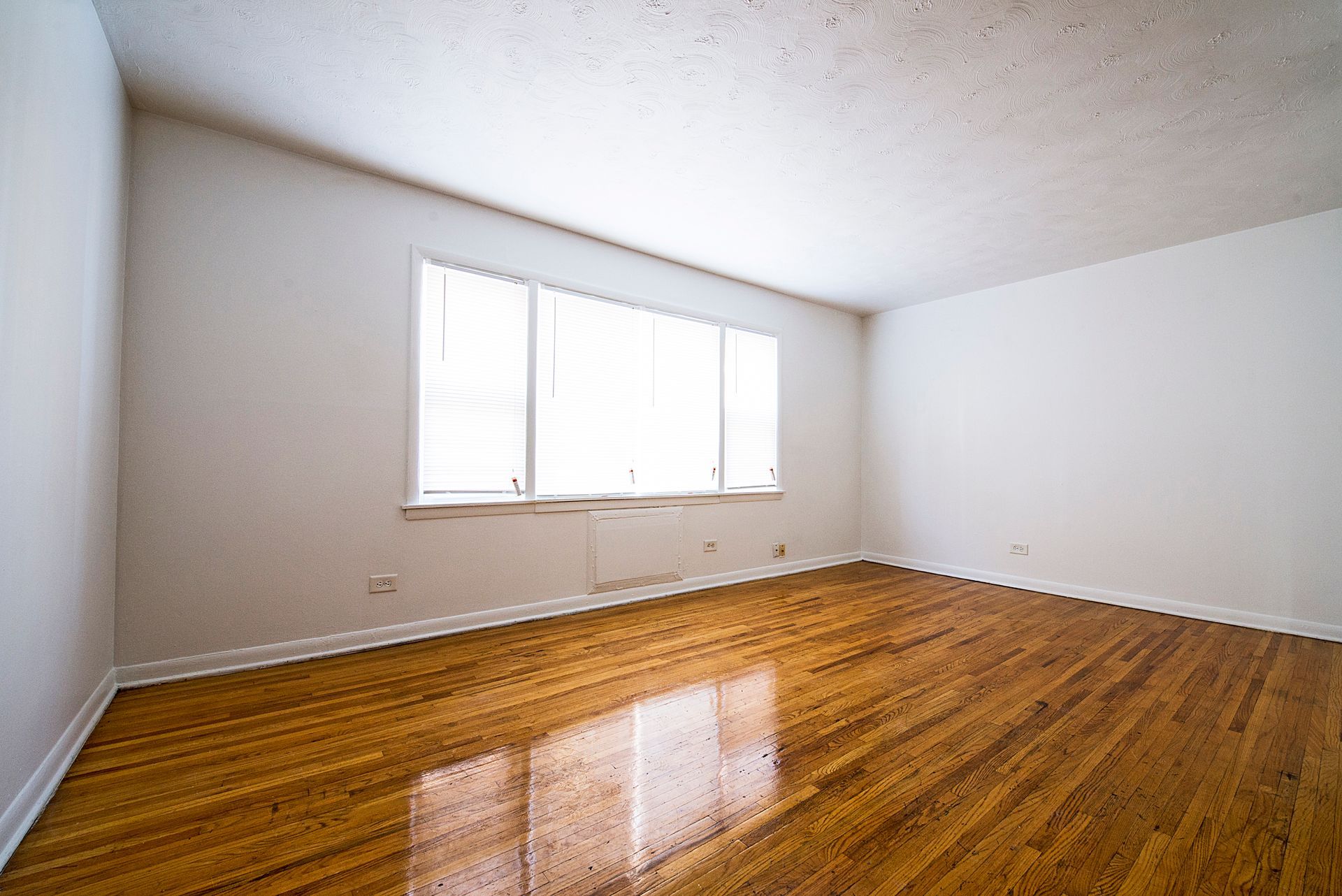 Empty room with wood floor, white walls, and a window with blinds.