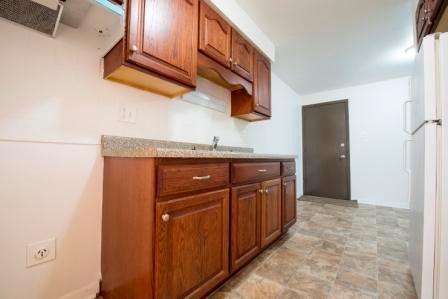 Kitchen with brown cabinets, gray countertop, white appliances, and brown door.