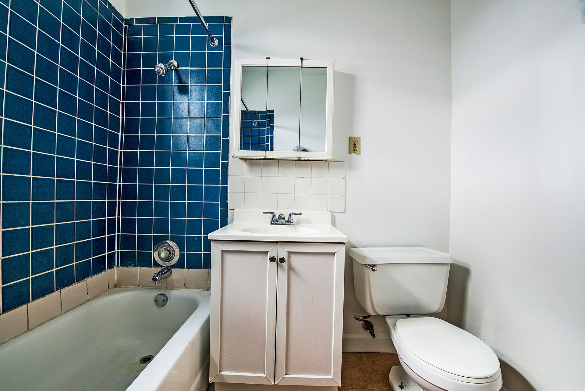 Bathroom with blue tile shower, white vanity, and toilet.