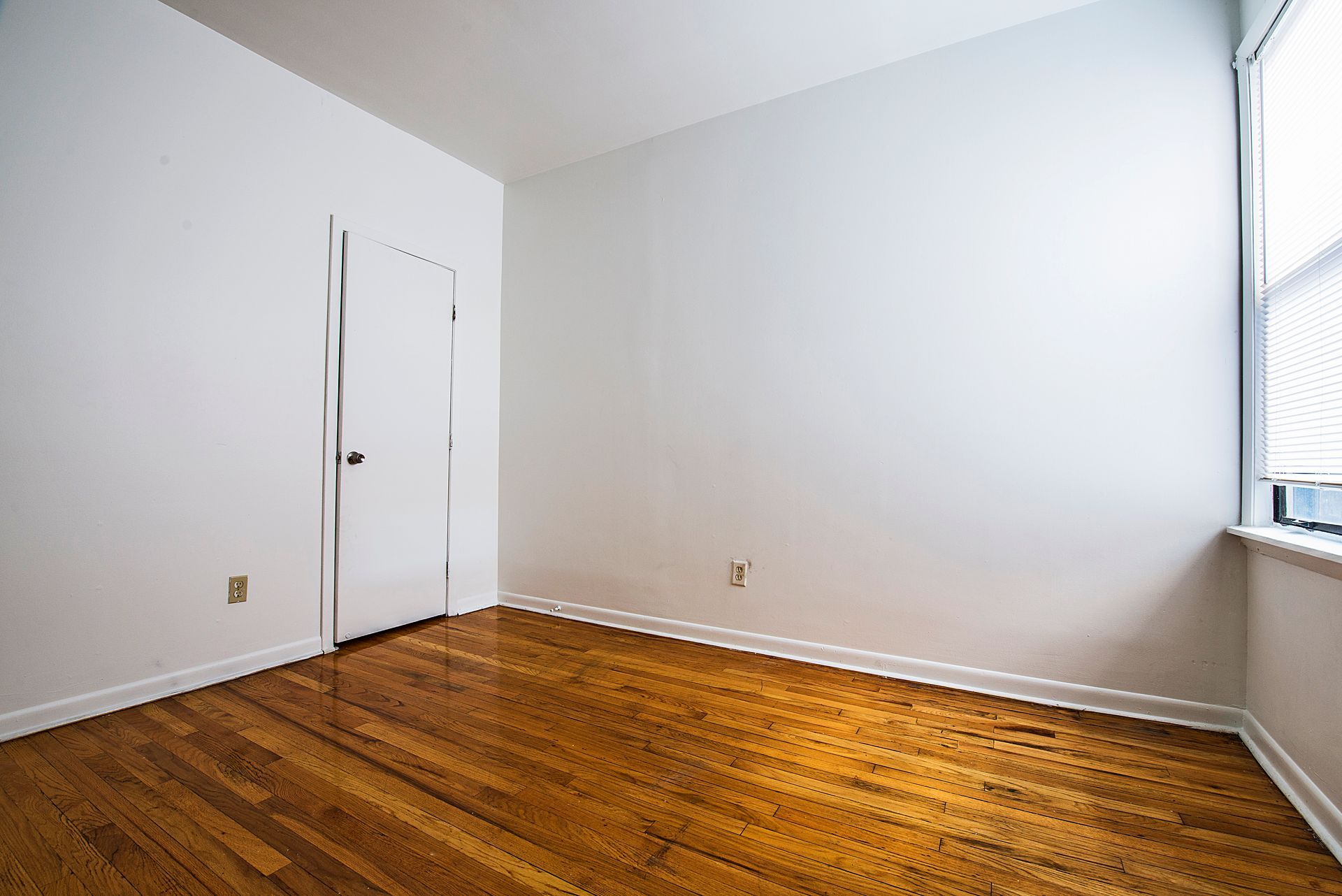 Empty room with hardwood floors, white walls, closet door, and window with blinds.