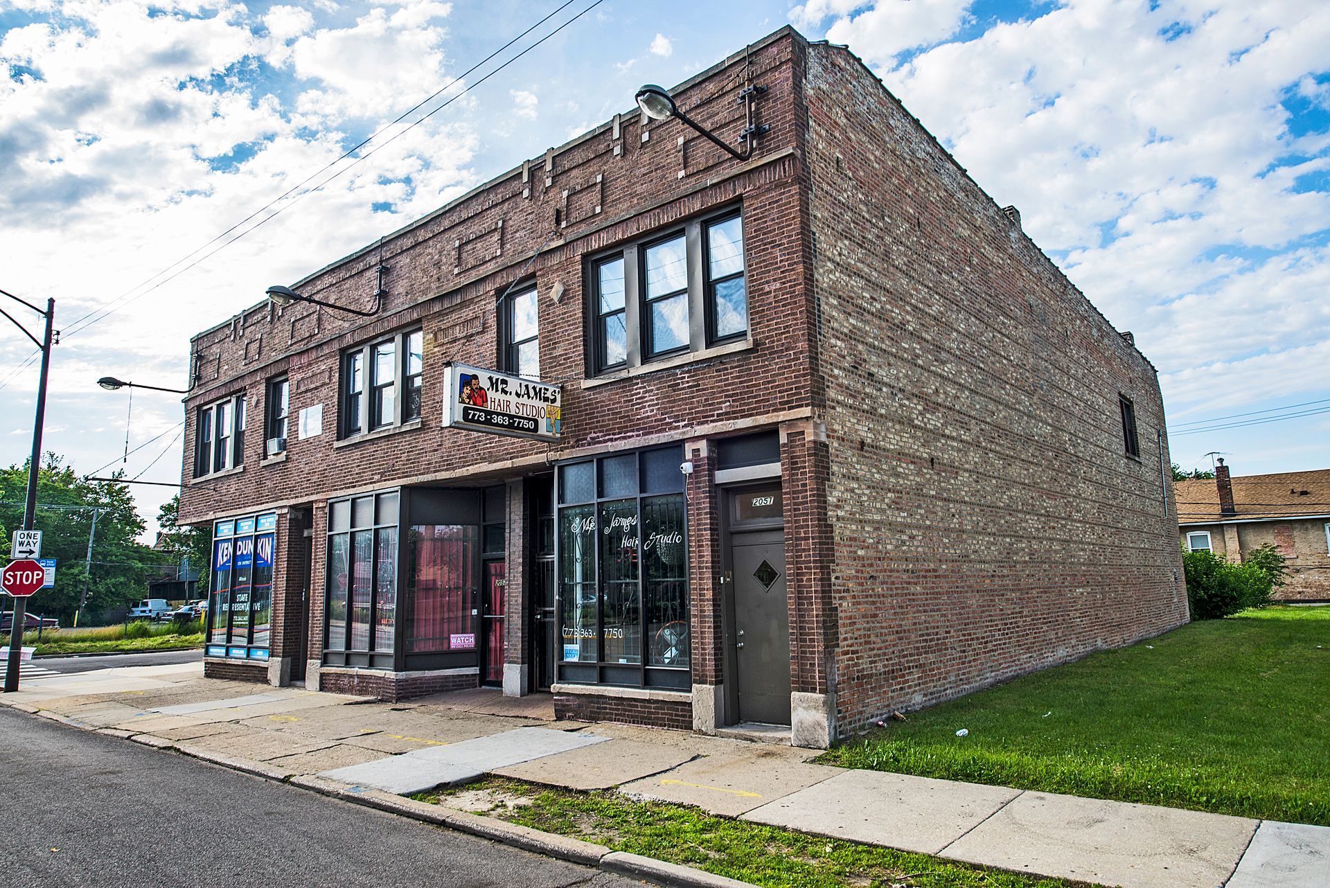 Two-story brick building with storefronts and a sidewalk in front. Cloudy sky overhead.