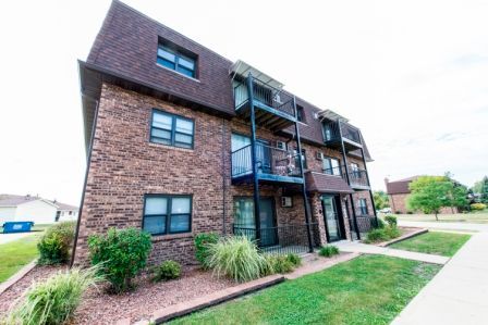 Brick apartment building with balconies, brown roof, and green lawn.