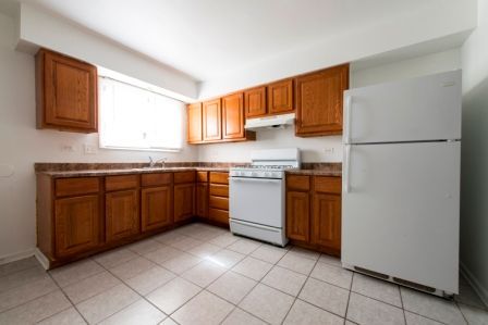 Kitchen with wooden cabinets, white appliances, and tiled floor.