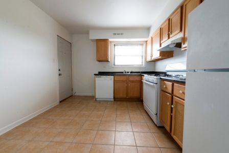 Empty kitchen with tile floor, light wood cabinets, and white appliances.