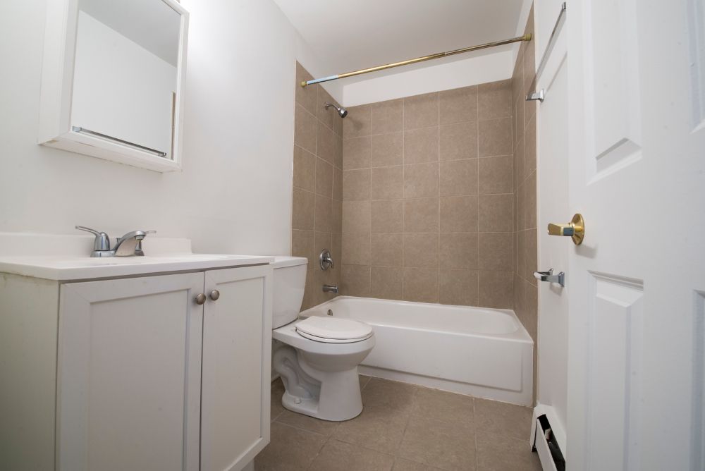 White bathroom with vanity, toilet, and bathtub. Beige tiled shower, white door.