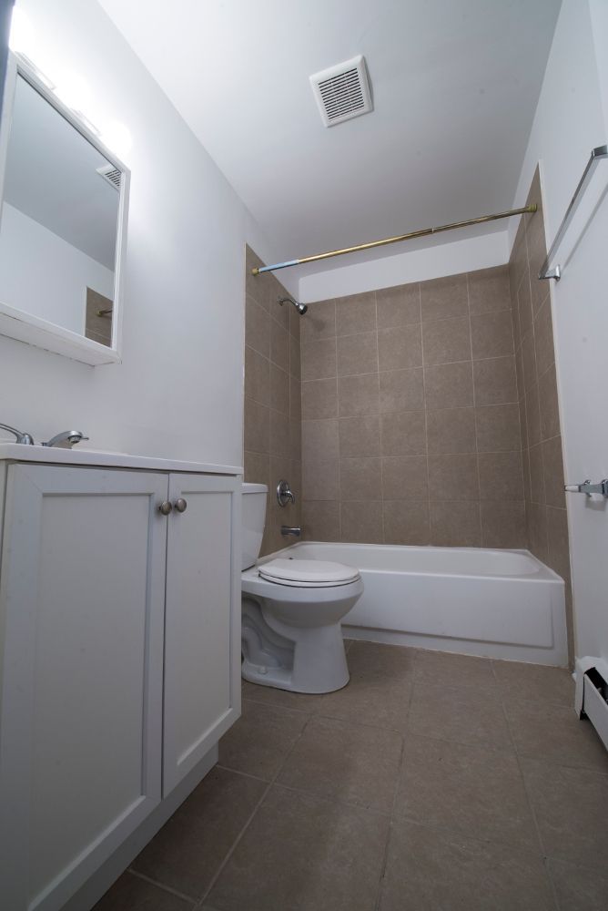 White bathroom with a bathtub, toilet, vanity, and tan-colored tile.