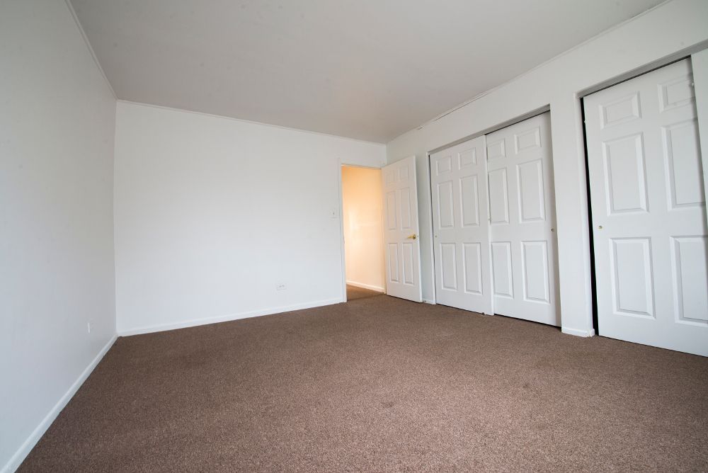 Empty room with brown carpet, white walls, and two closets. Open doorway in background.