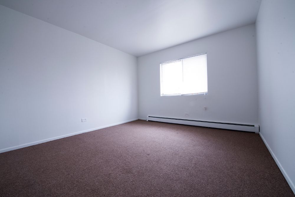 Empty room with brown carpet, white walls, and a window with blinds.