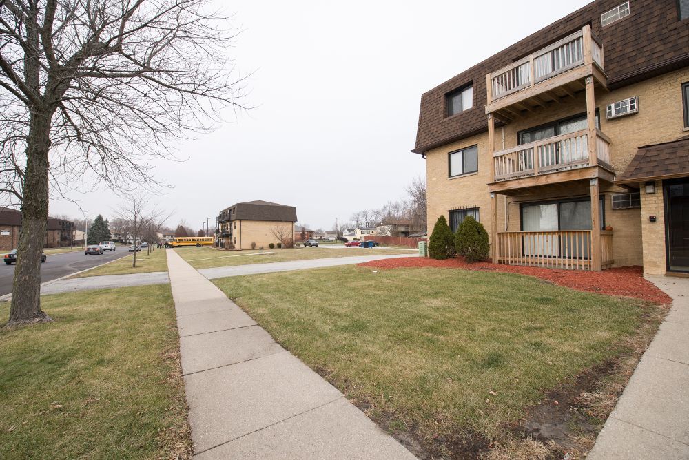 Apartment building with balconies and sidewalk, lawn, street, overcast sky.