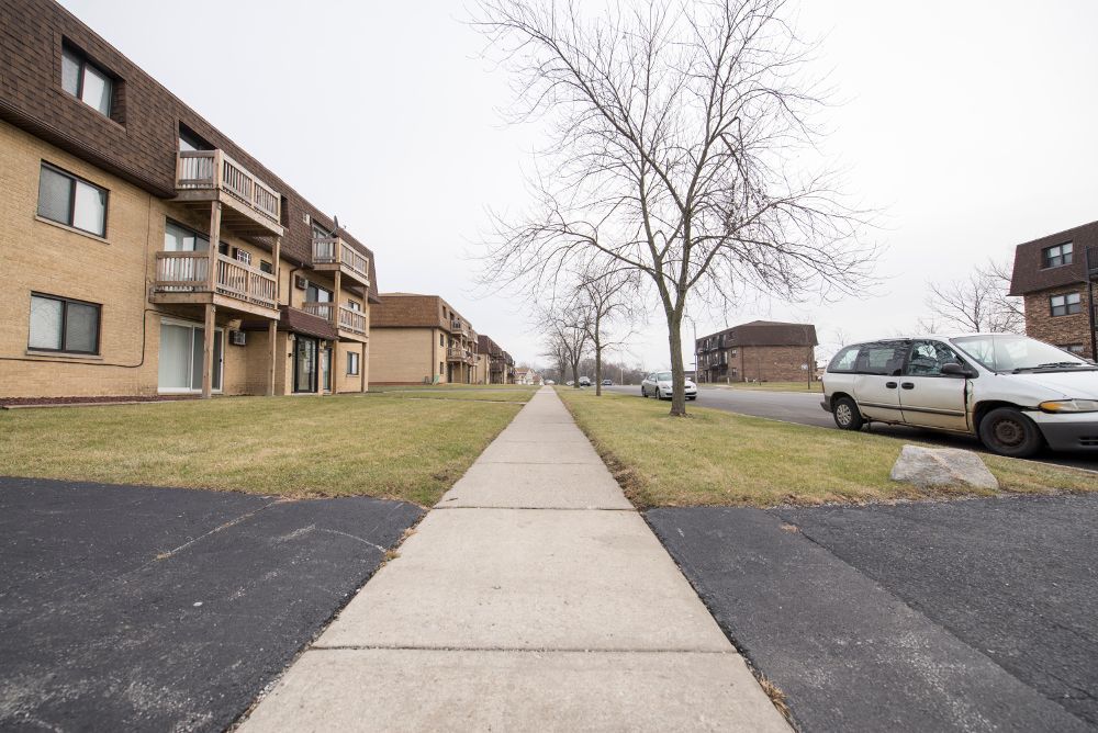 Sidewalk through apartment complex on a cloudy day, van parked on the side.