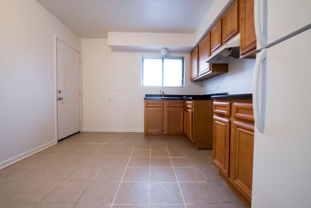 Empty kitchen with wooden cabinets, a window, and a white refrigerator.