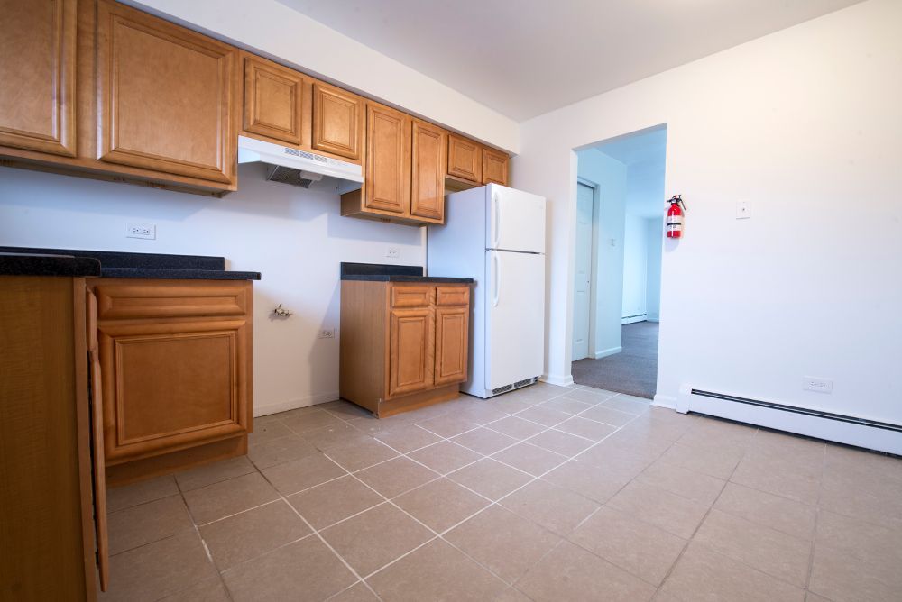 Kitchen with light brown cabinets, black countertops, white refrigerator, and tiled floor.