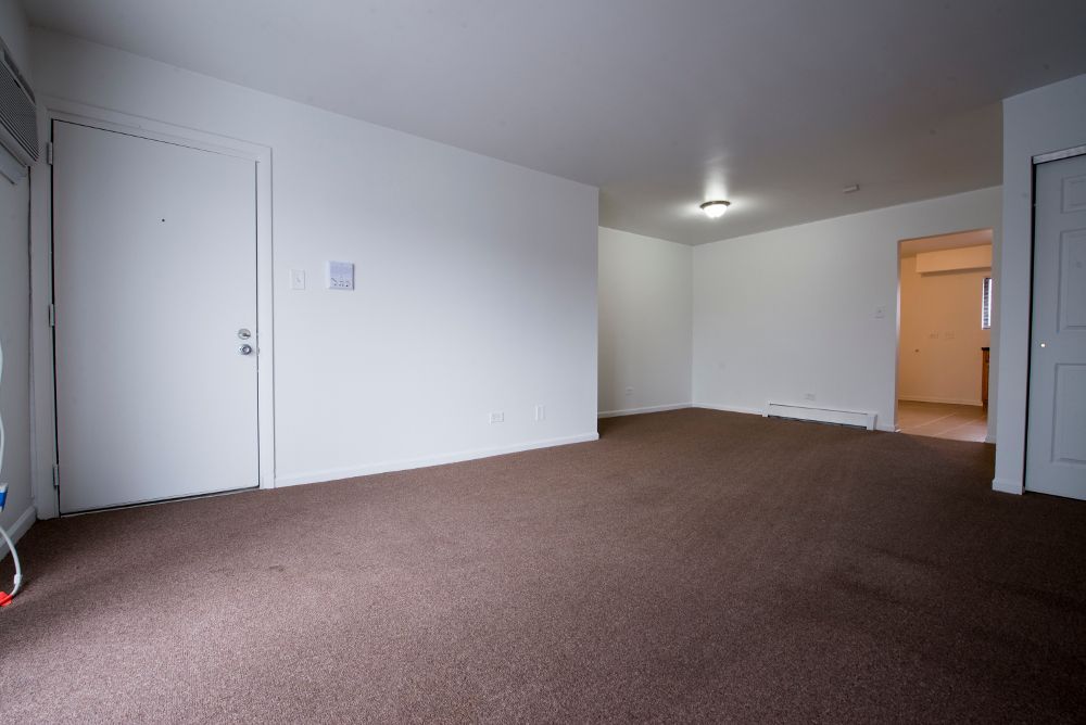 Empty room with brown carpet, white walls, two doors, and an open doorway.