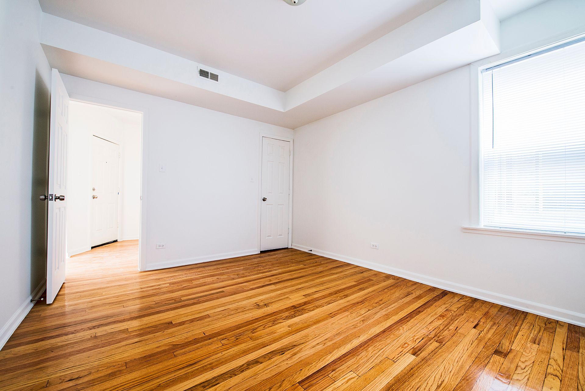 Empty room with hardwood floors, white walls, and a window with blinds.