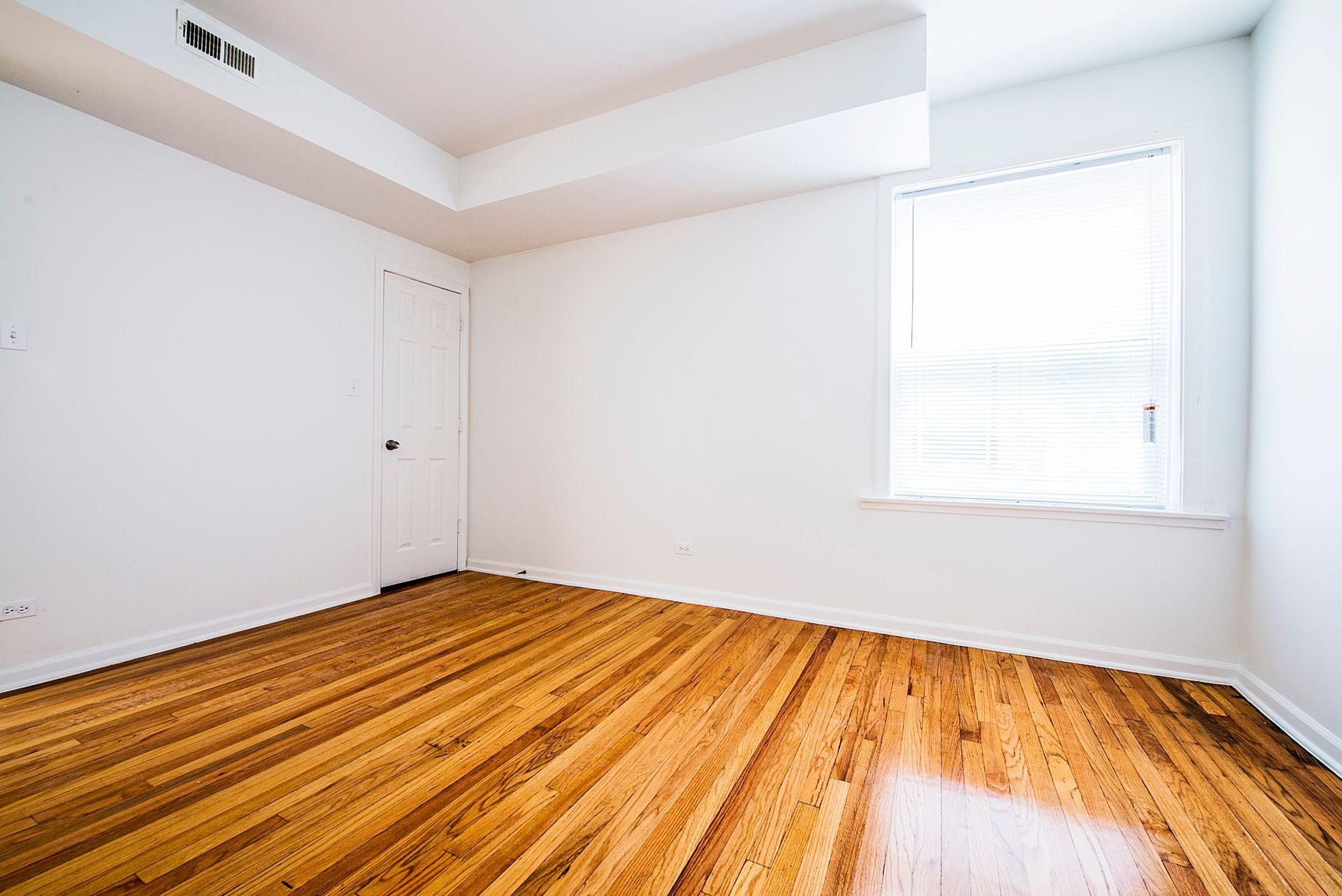Empty room with wood floors, white walls, door, window with blinds.