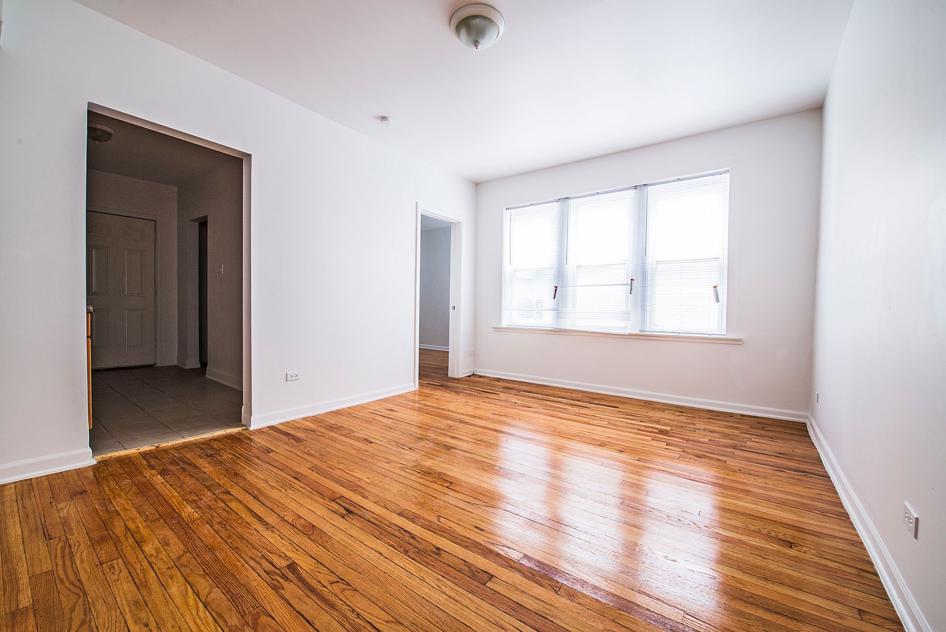Empty room with hardwood floors, white walls, and a window.