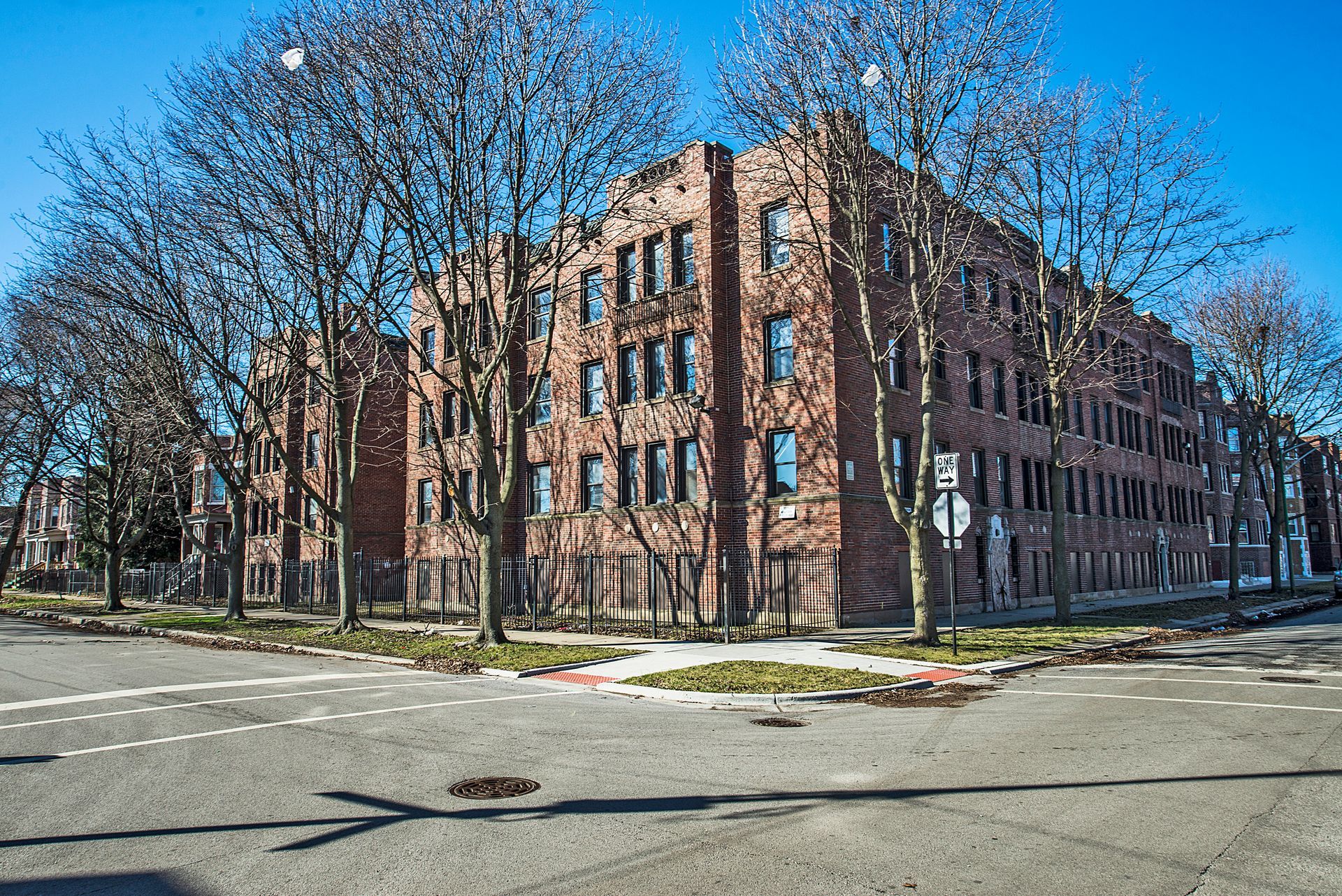 Brick apartment building on a street corner, surrounded by bare trees, sunny day.