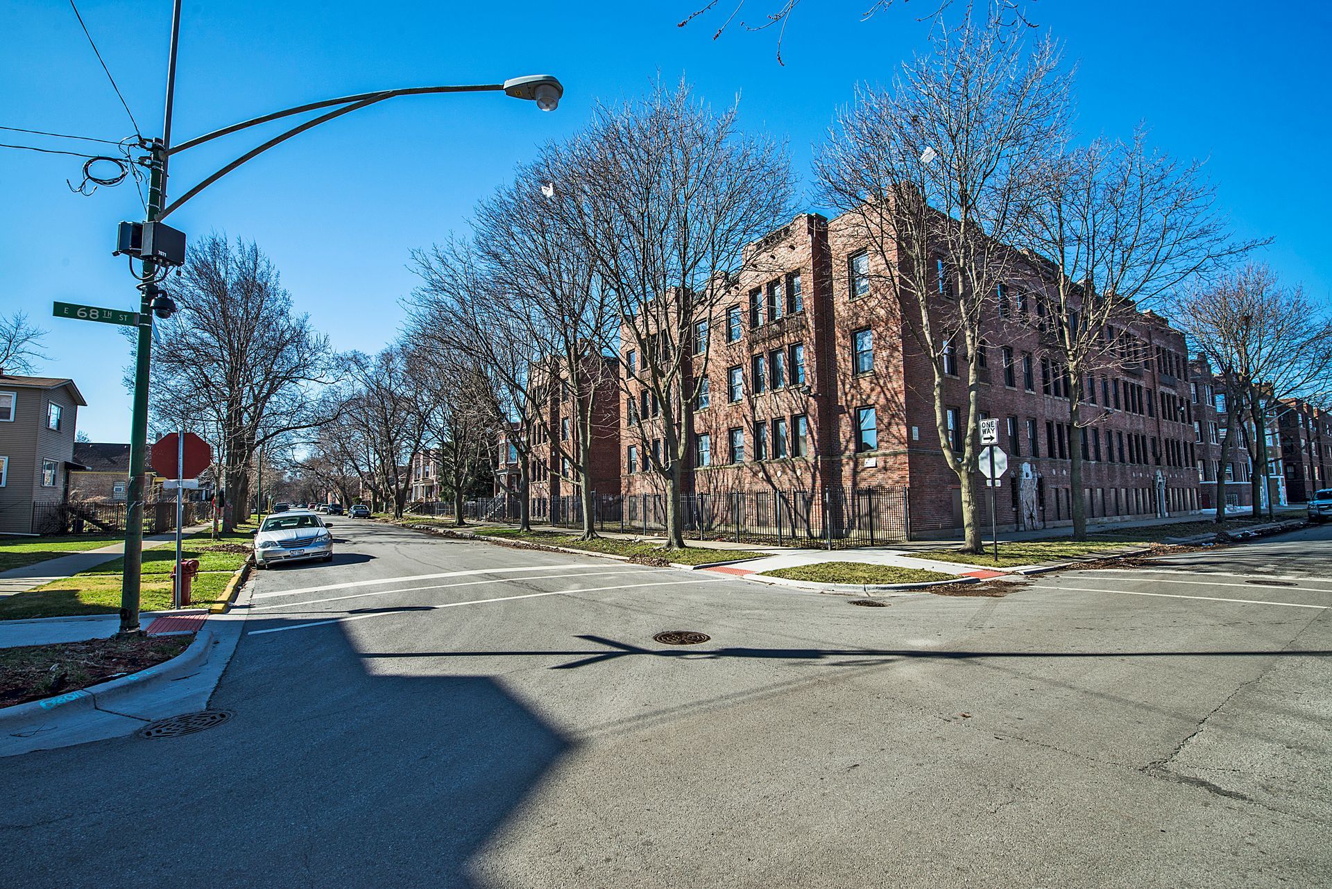 Brick apartment building at a street corner on a sunny day with trees.