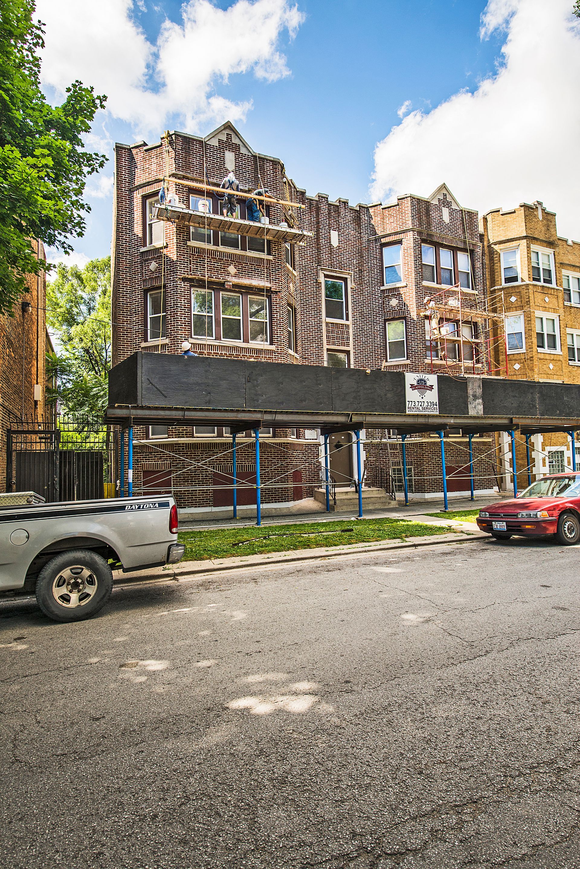 Brick building covered in vines, behind a black fence, blue sky.
