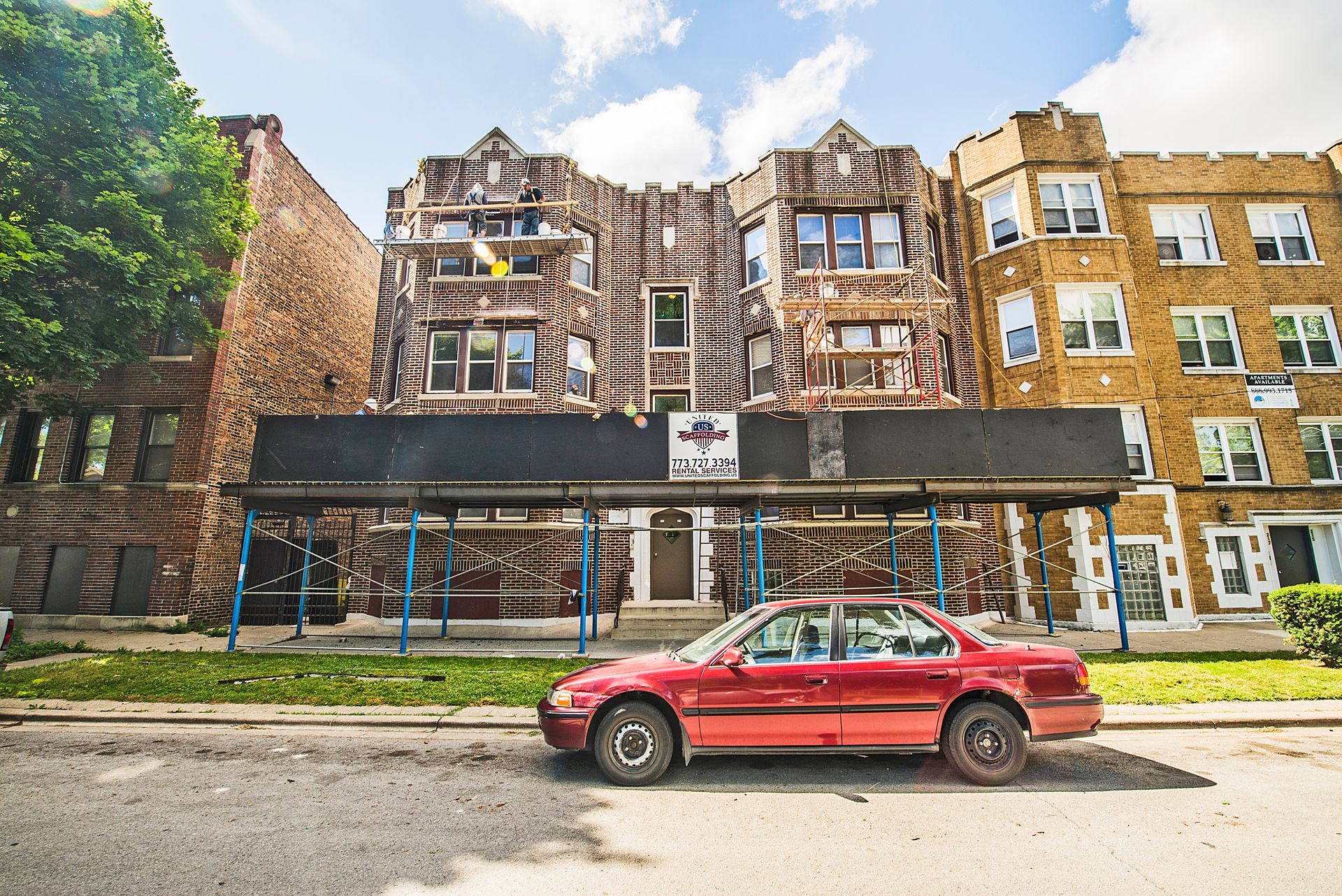 Red car parked in front of a brick building with weathered facade, sunny day.