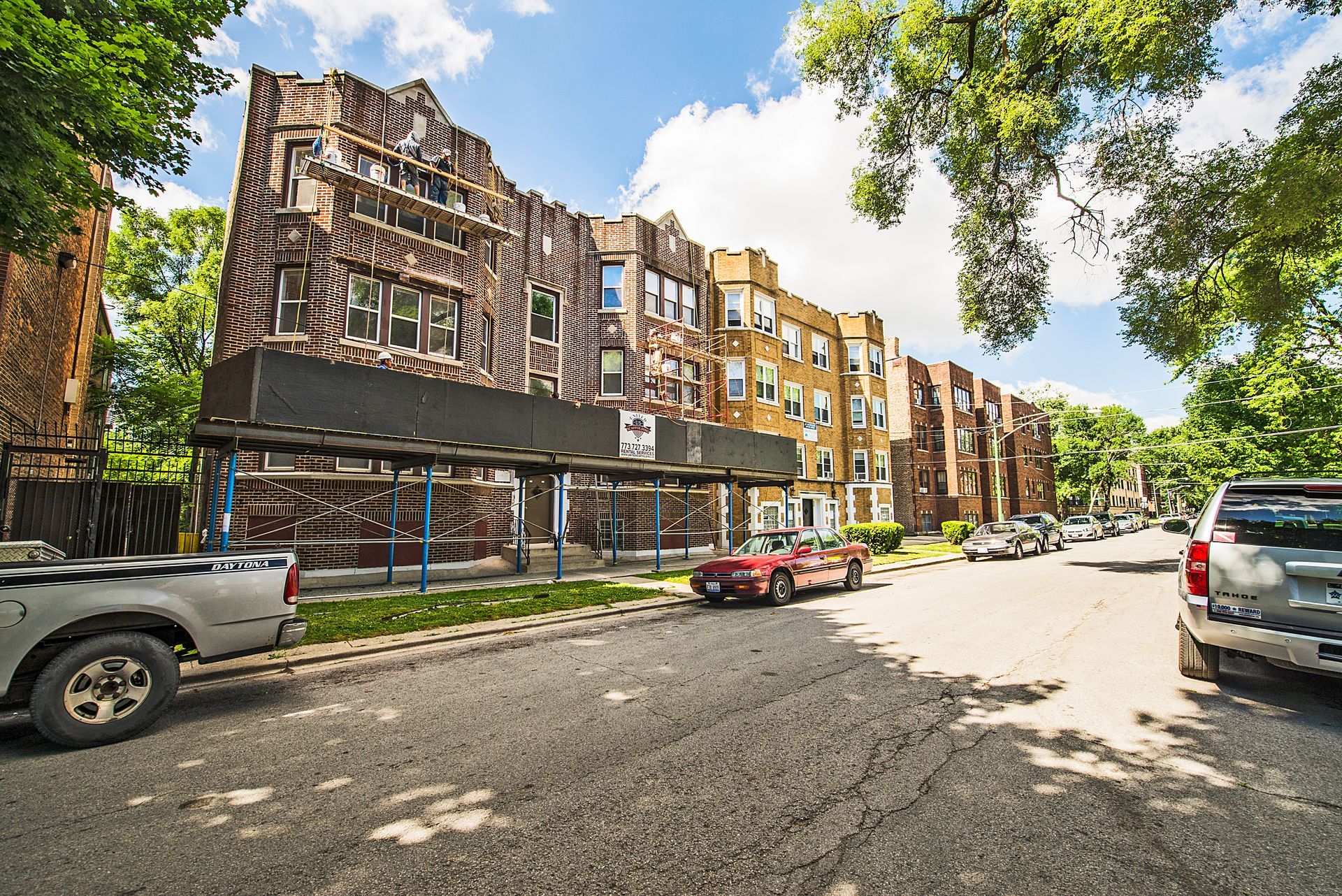 Apartment buildings with a large mural, a street, cars, and trees on a sunny day.