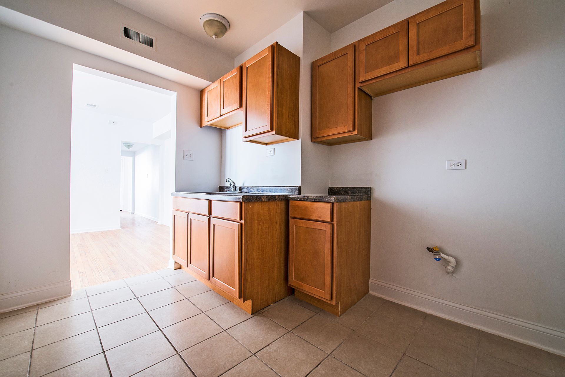Kitchen with wooden cabinets and tiled floor. Open doorway leads to another room.