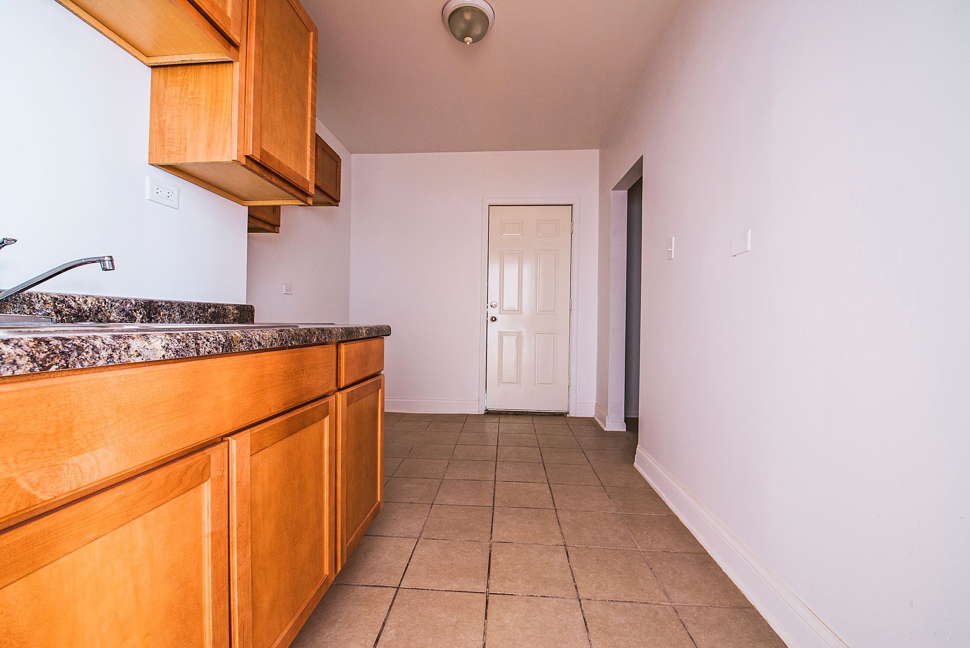 Kitchen with light brown cabinets, marble countertop, white walls, and a door.