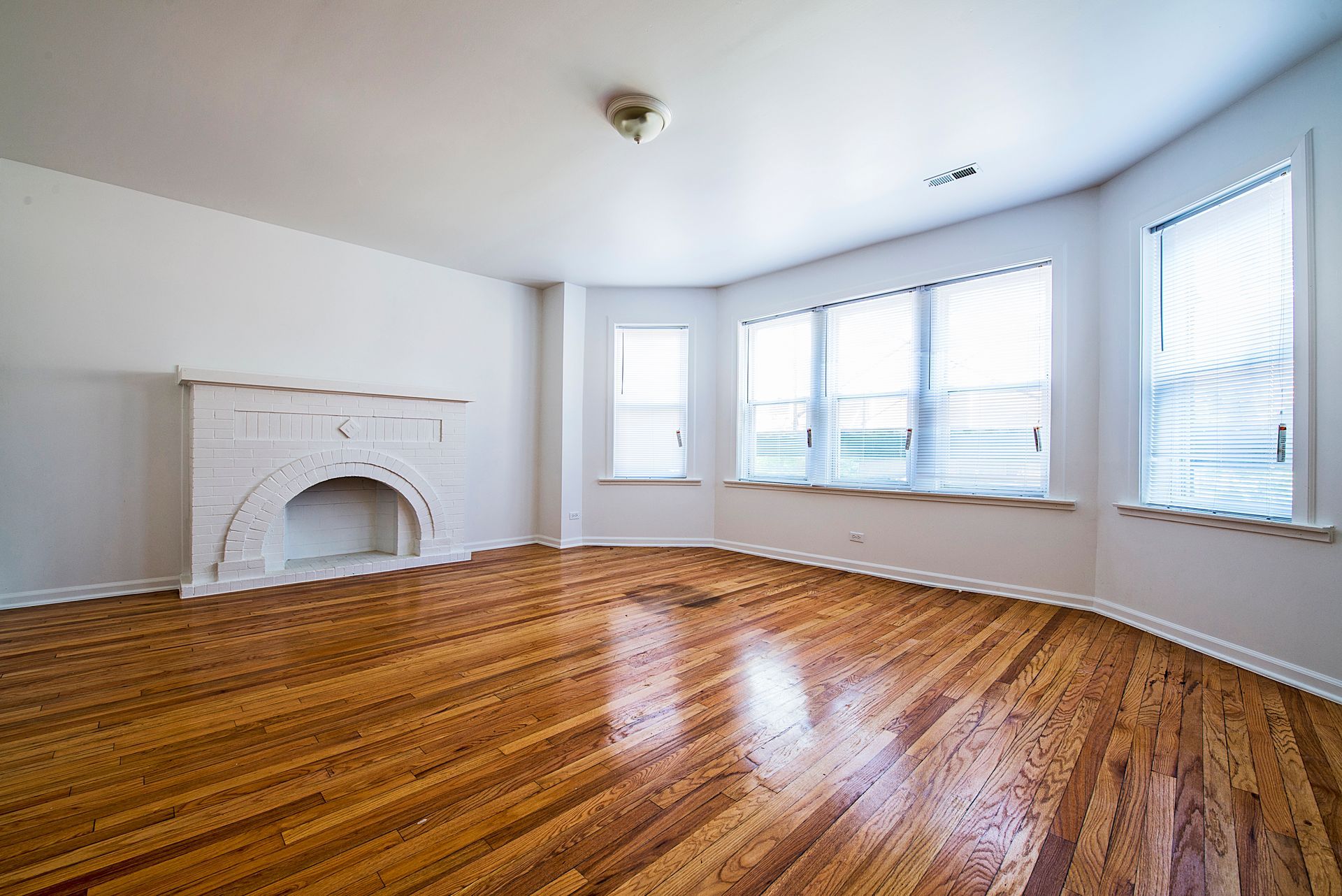 Empty living room with wood floors, fireplace, and windows.