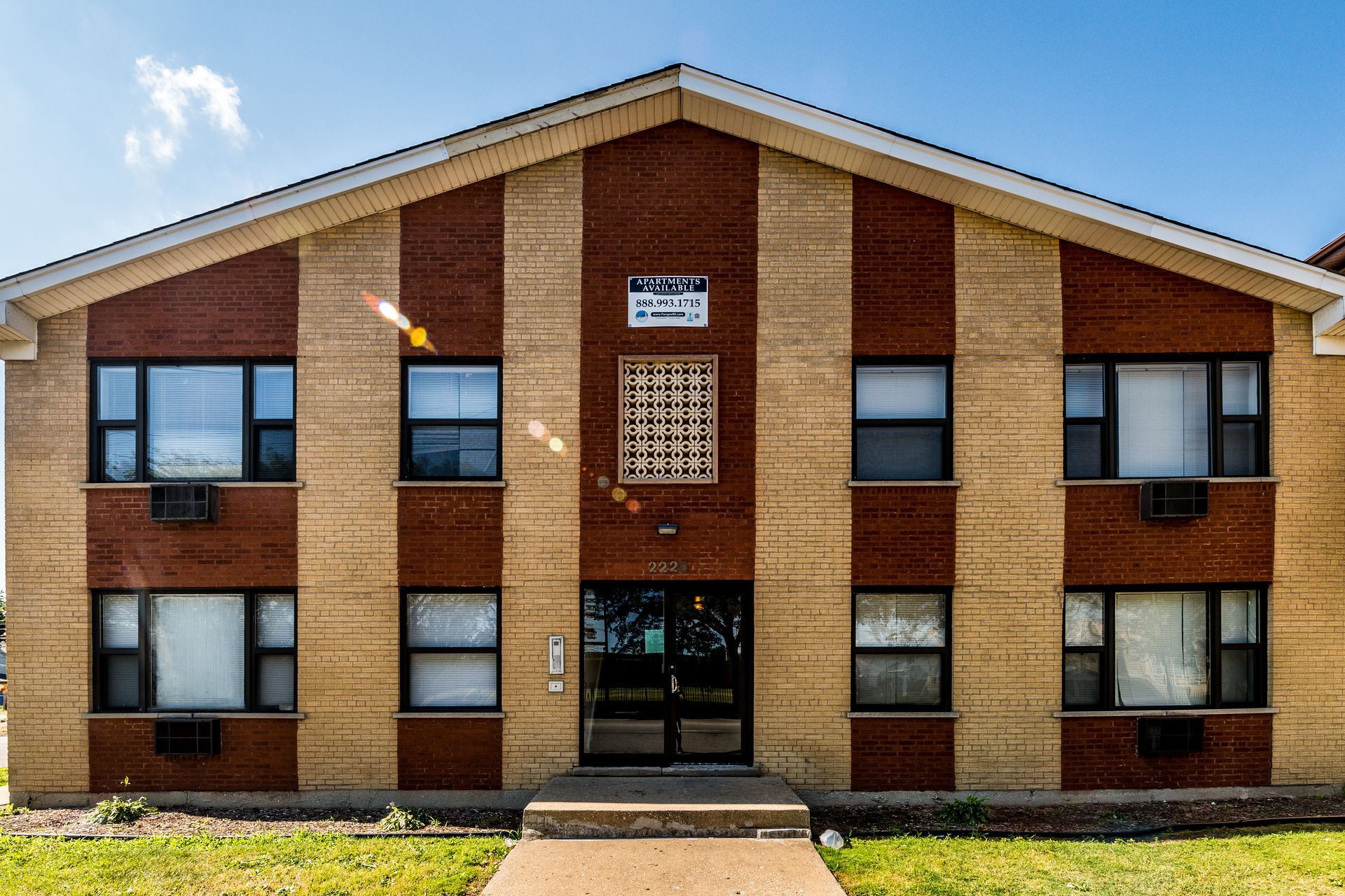 Two-story brick building with alternating tan and dark red vertical stripes, multiple windows, and a central entrance.