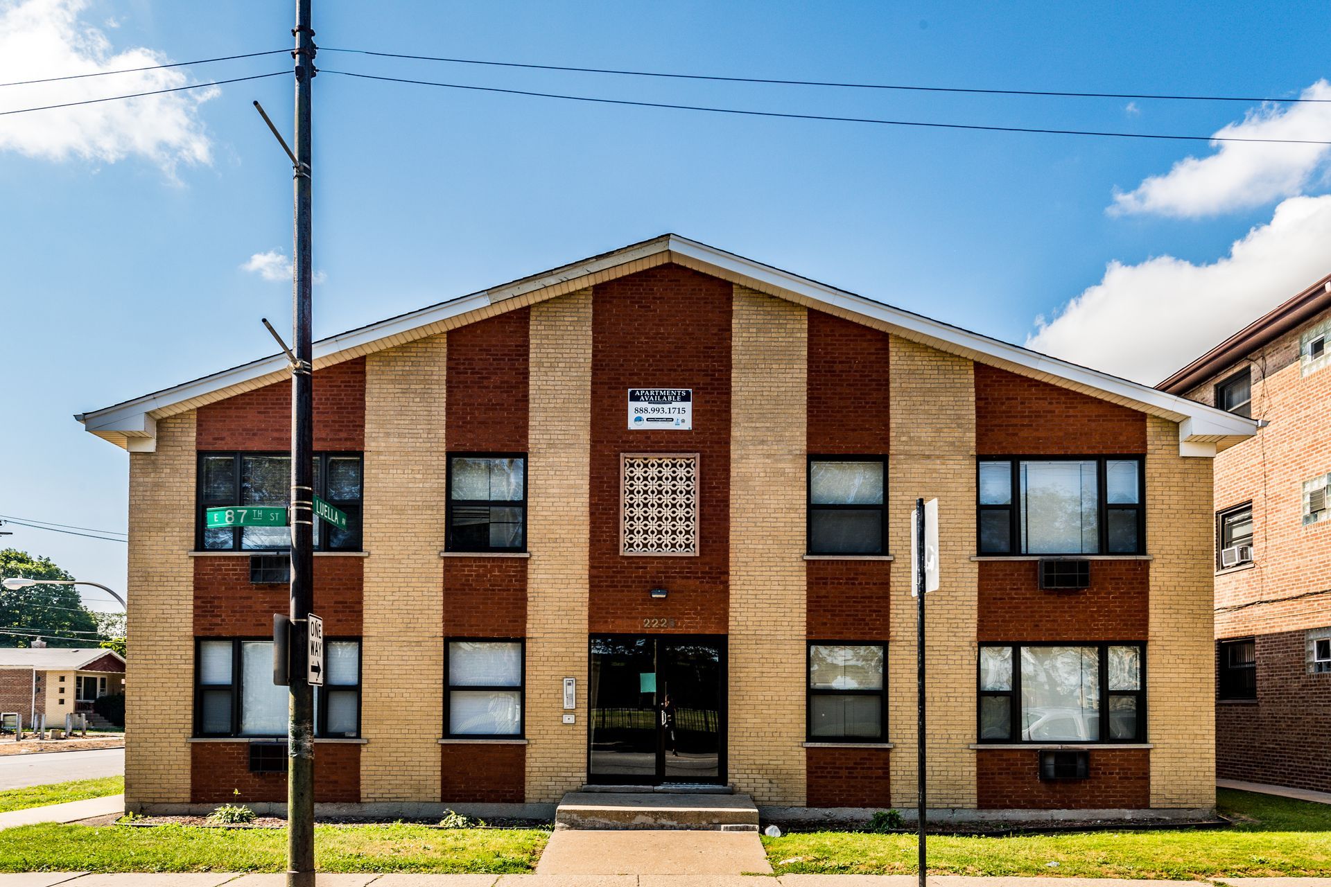 Two-story brick apartment building with alternating red and tan vertical stripes, under a clear sky.