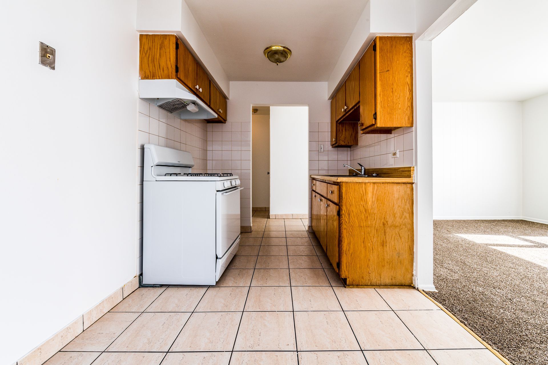 Kitchen with white appliances, wooden cabinets, and tile floor.