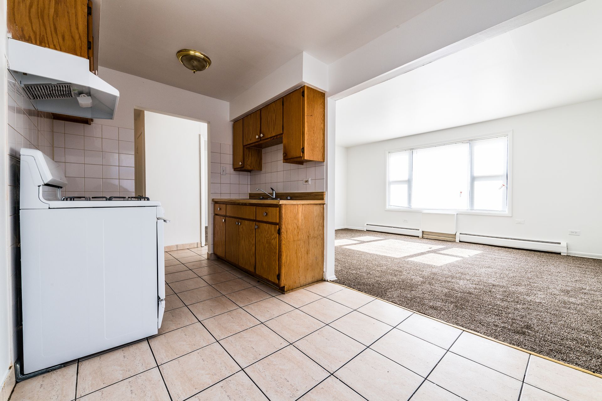 Kitchen with stove, cabinets, and a doorway opening into a carpeted living room with a large window.