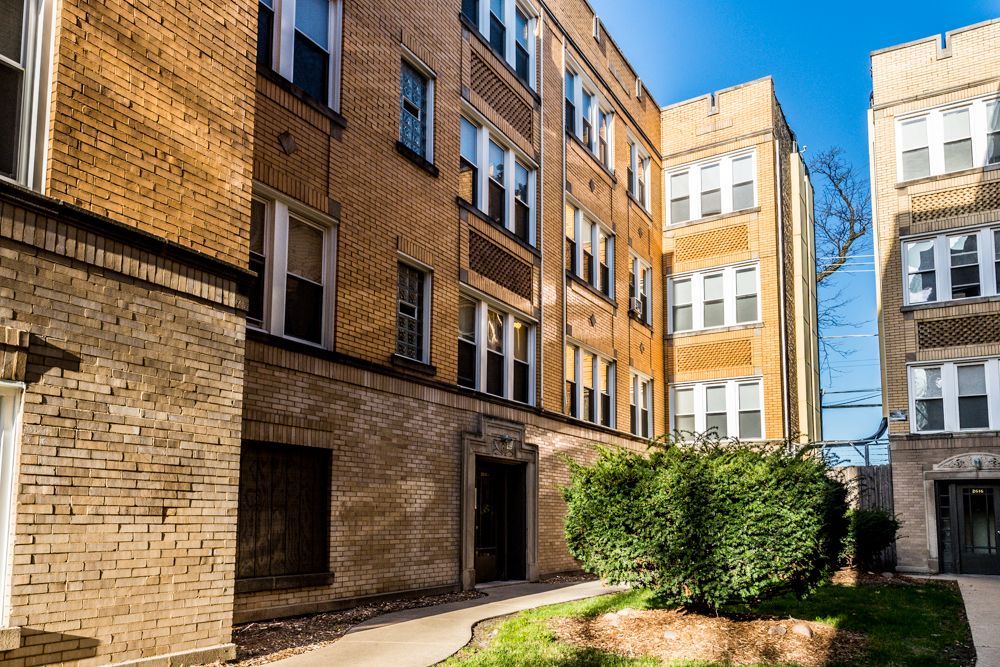 Apartment buildings with brick exteriors and multiple windows, viewed from an outdoor pathway, on a sunny day.