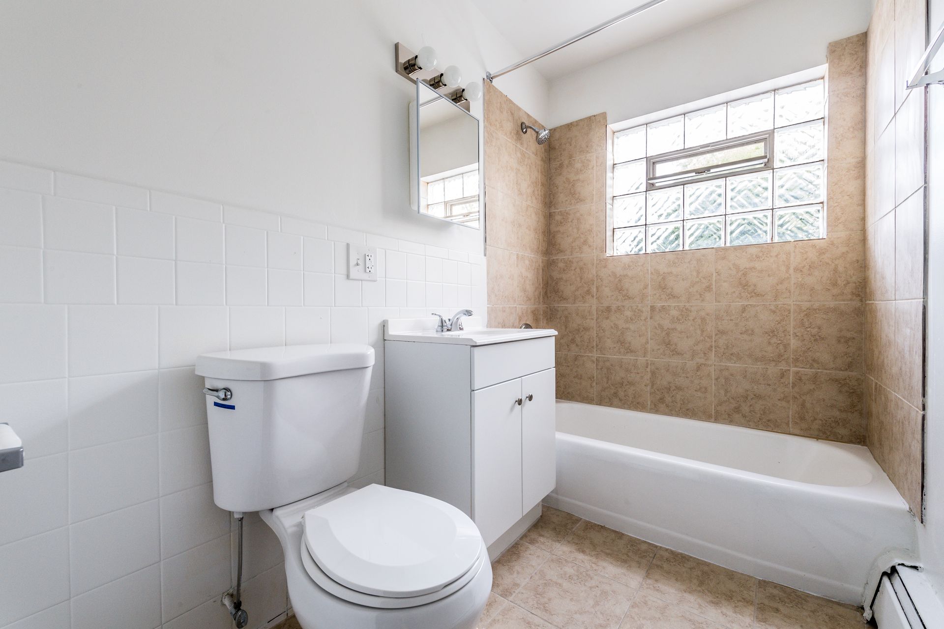 Bathroom with white toilet and vanity, beige tiled tub surround, and square block window.