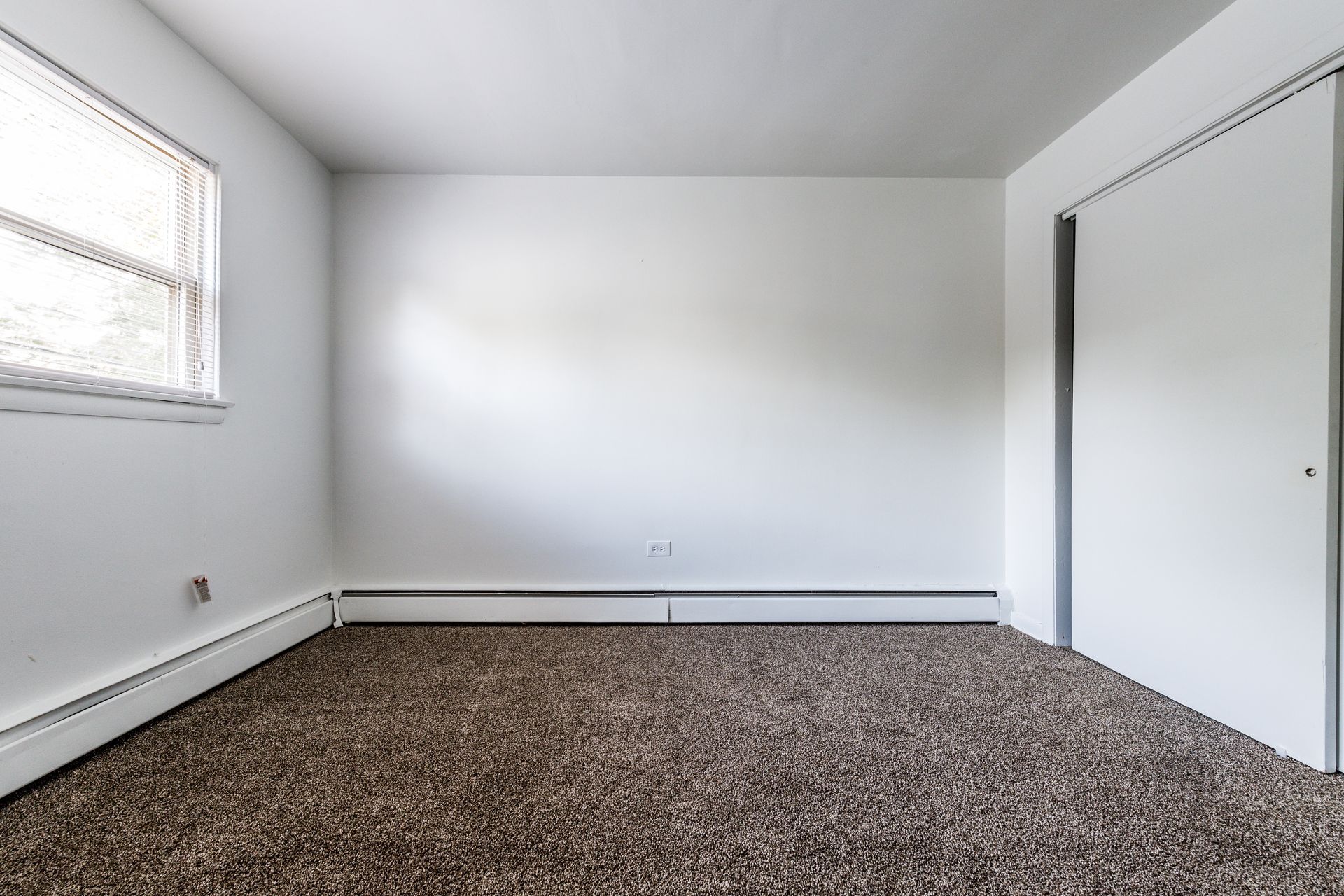 Empty room with white walls, brown carpet, window, and closet.