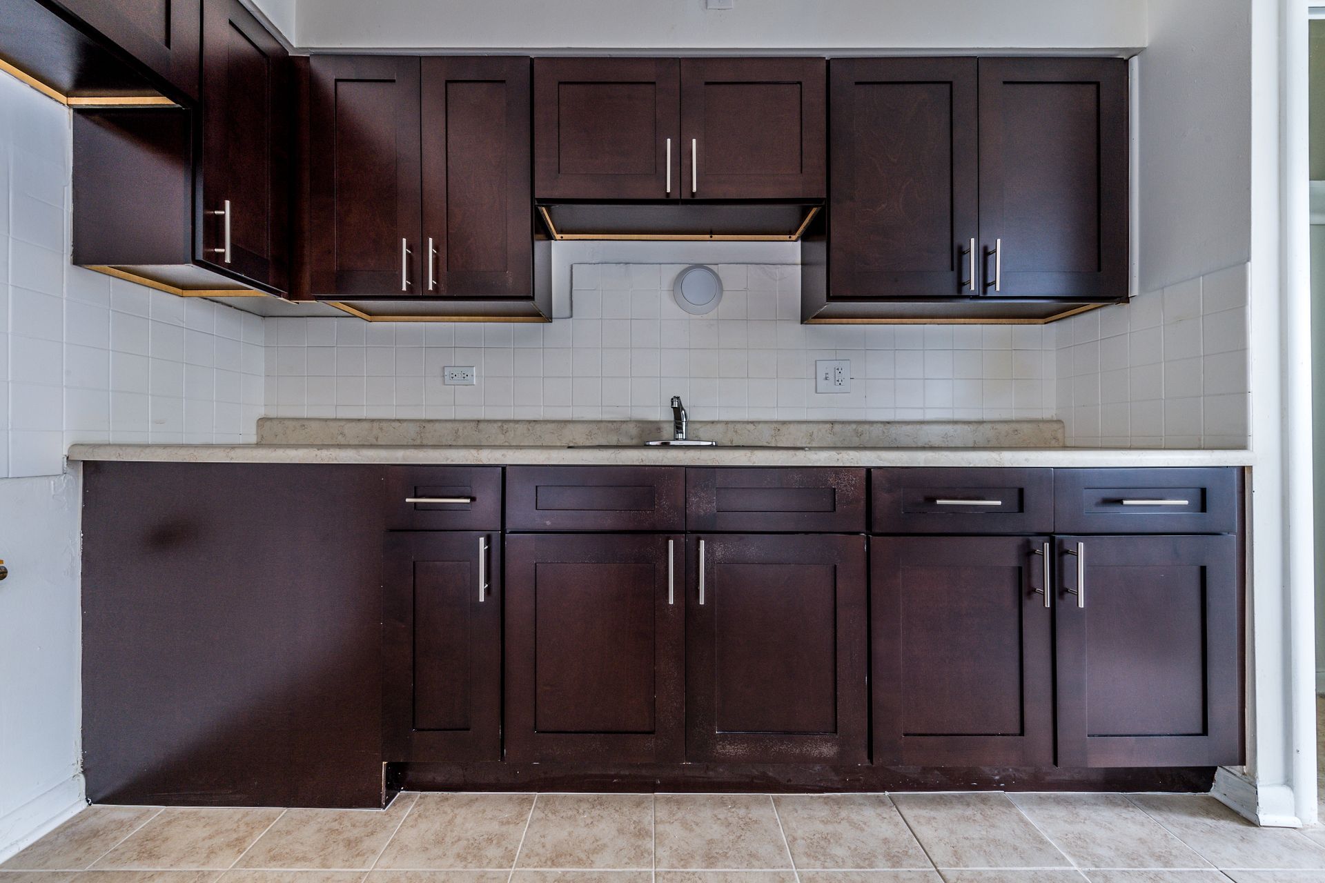 Dark brown kitchen cabinets with a light countertop and white tile backsplash.