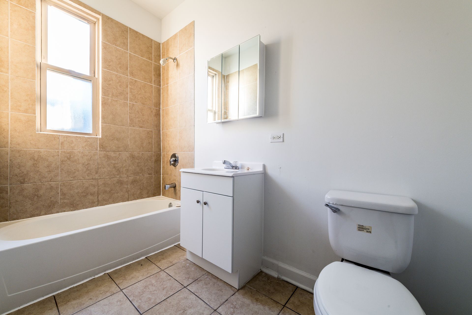 Bathroom with white fixtures, beige tile, and a window.