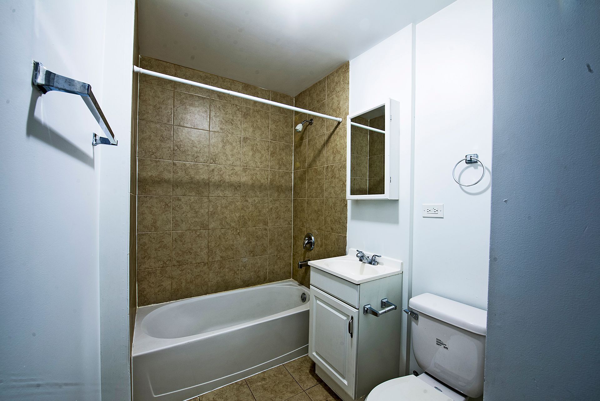 Small bathroom with a bathtub, toilet, vanity, and shower curtain. Beige tile and white fixtures.