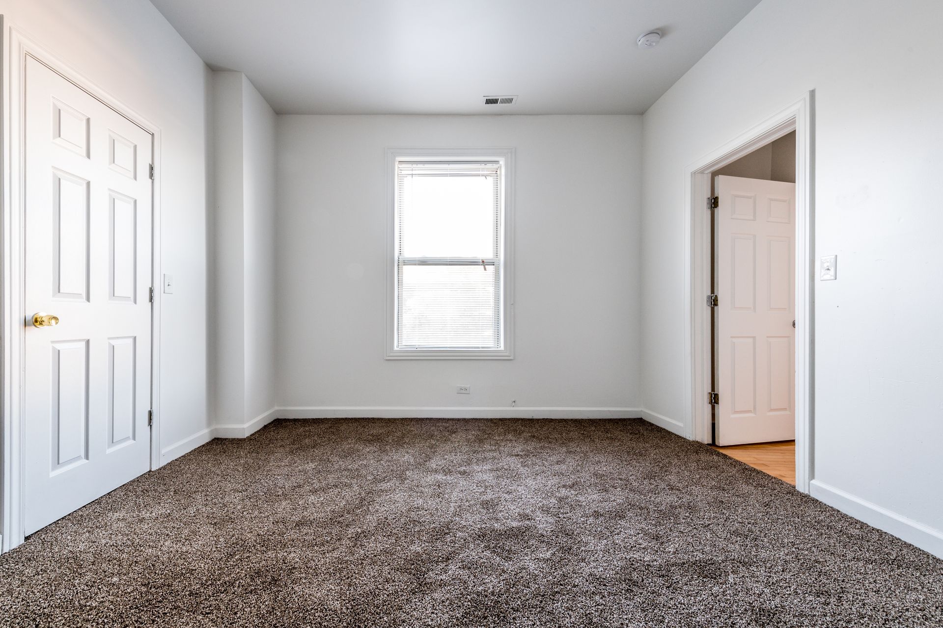 Empty room with brown carpet, white walls, and two closed doors.