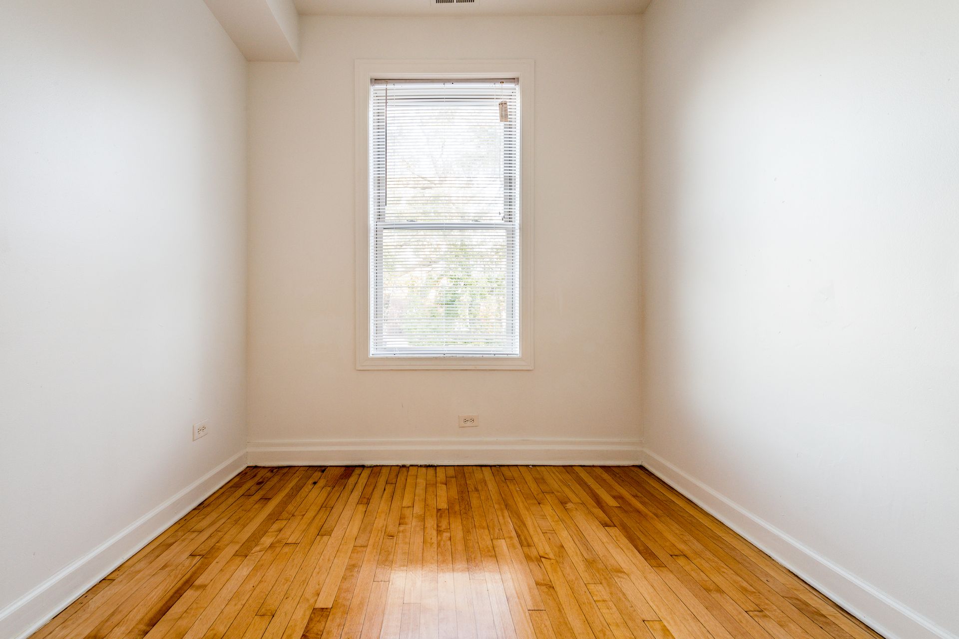 Empty room with hardwood floors, white walls, and a window with blinds.