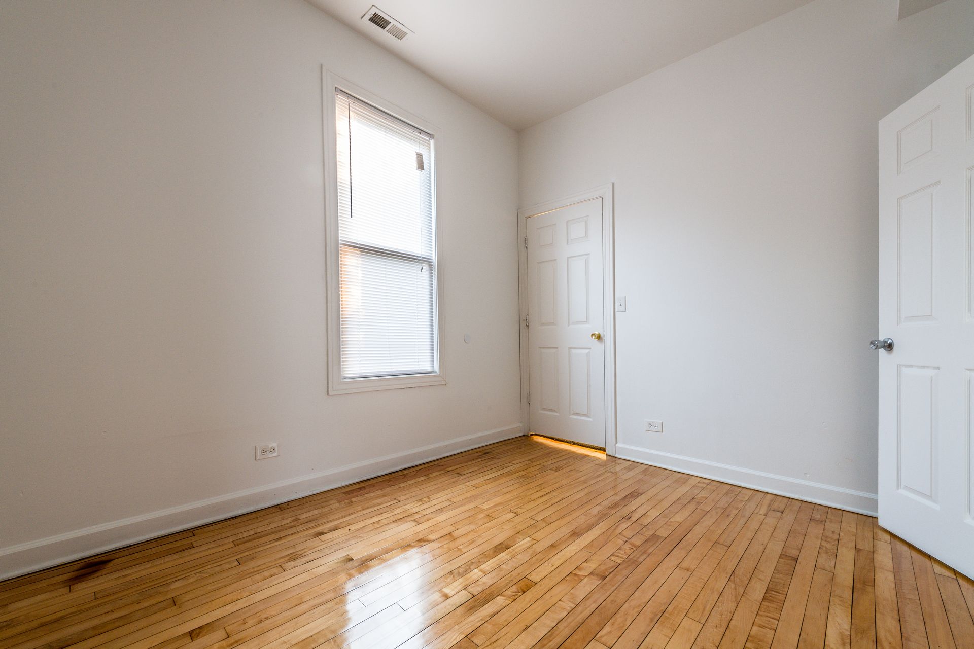 Empty room with hardwood floors, white walls, a window, and two doors.