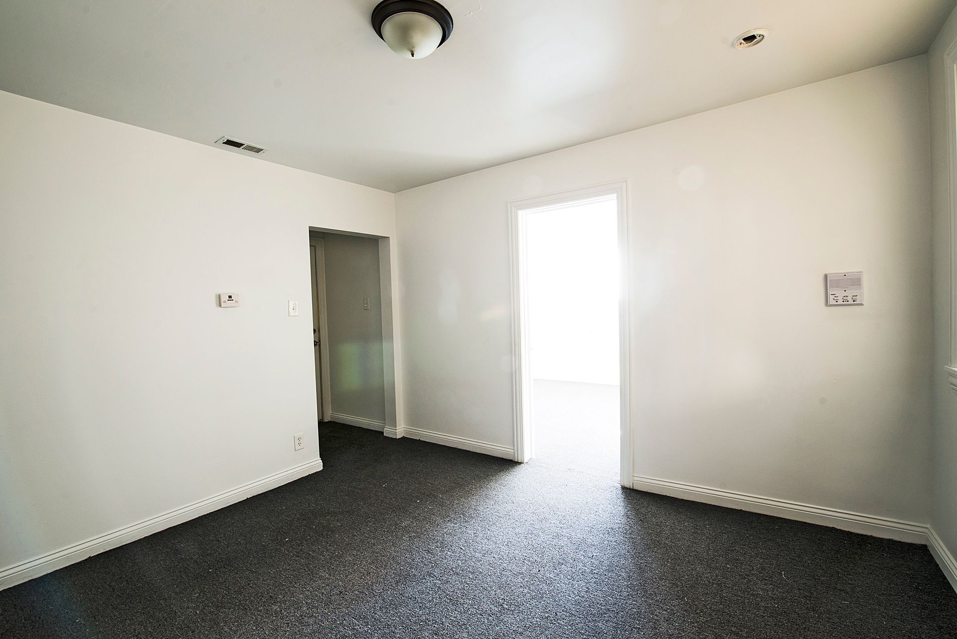 Empty room with gray speckled flooring, white walls, and bright doorway.