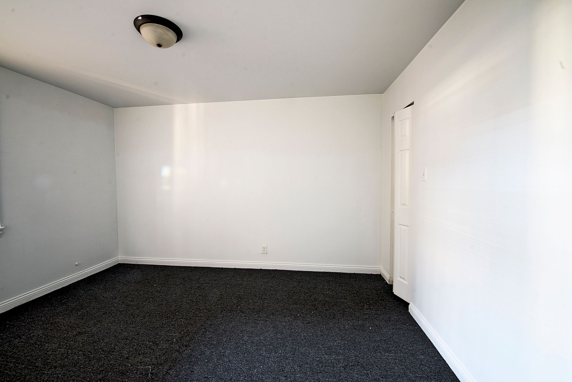 Empty room with white walls, black carpet, and a ceiling light.