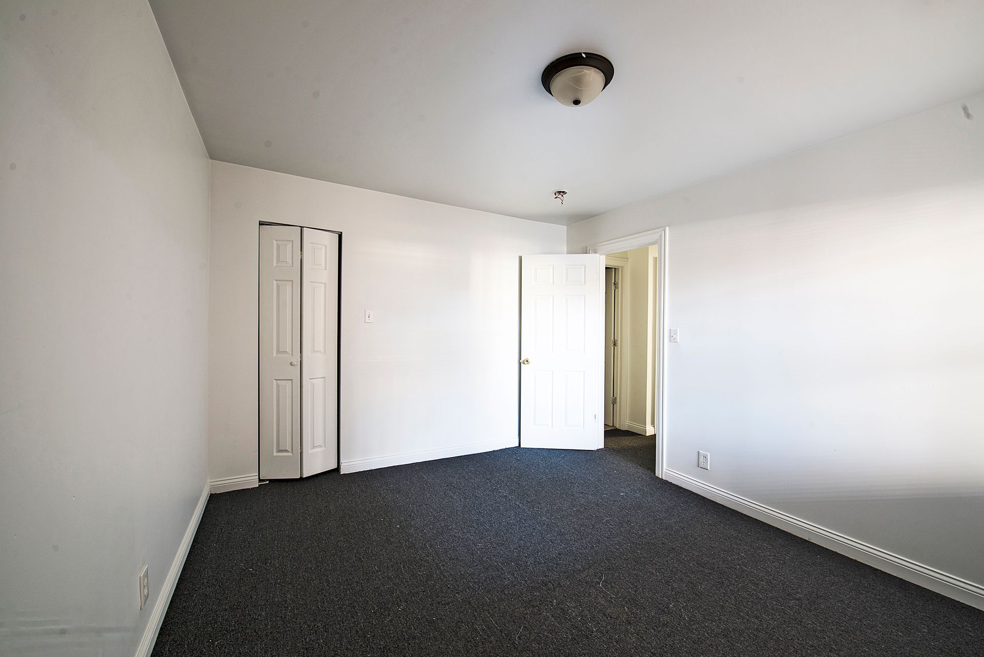 Empty room with dark gray carpet, white walls, and a closed bi-fold closet door.