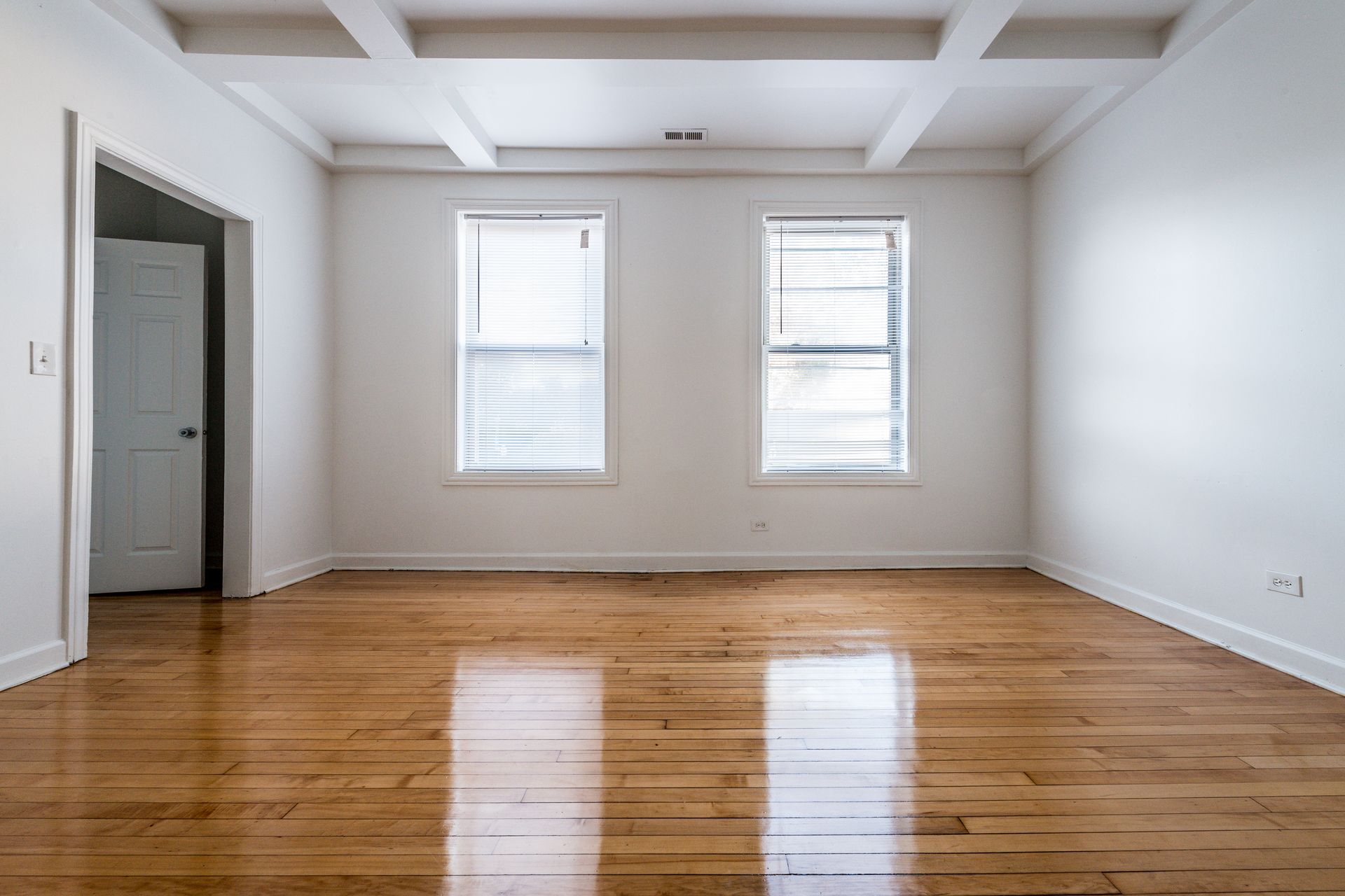 Empty room with hardwood floors, two windows, and white walls and ceiling.