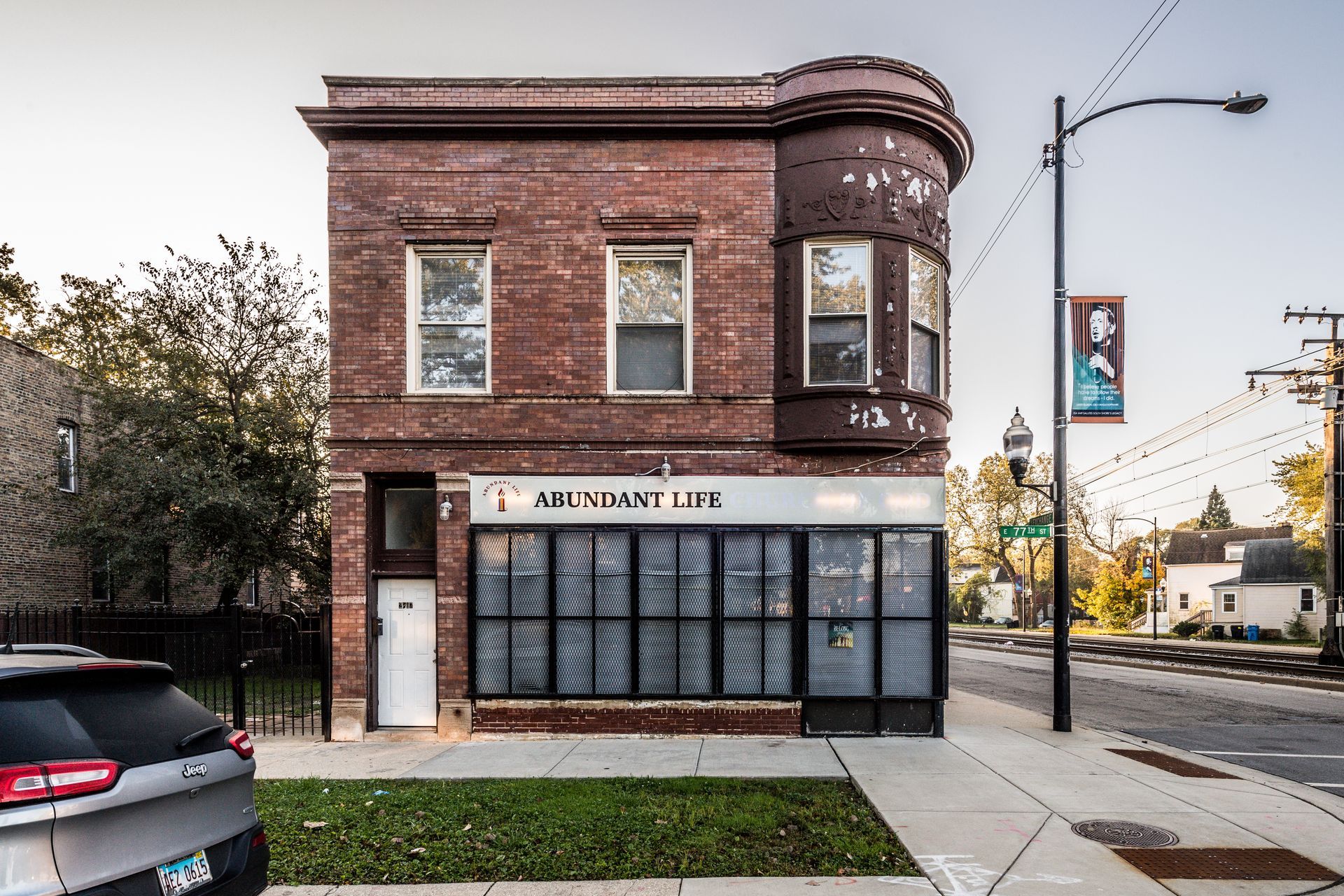 Brick building with a storefront. A car is parked in front, and a street light and poster are beside the building.