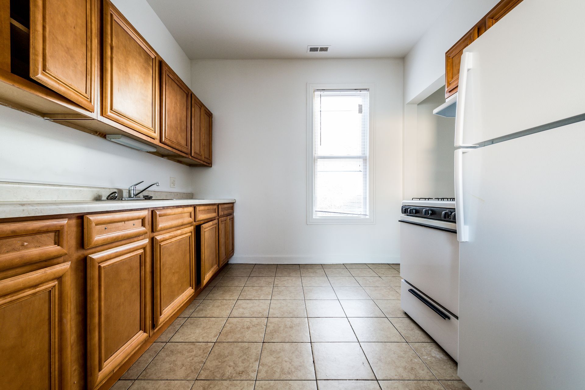 Empty kitchen with wood cabinets, white appliances, and tiled floor.