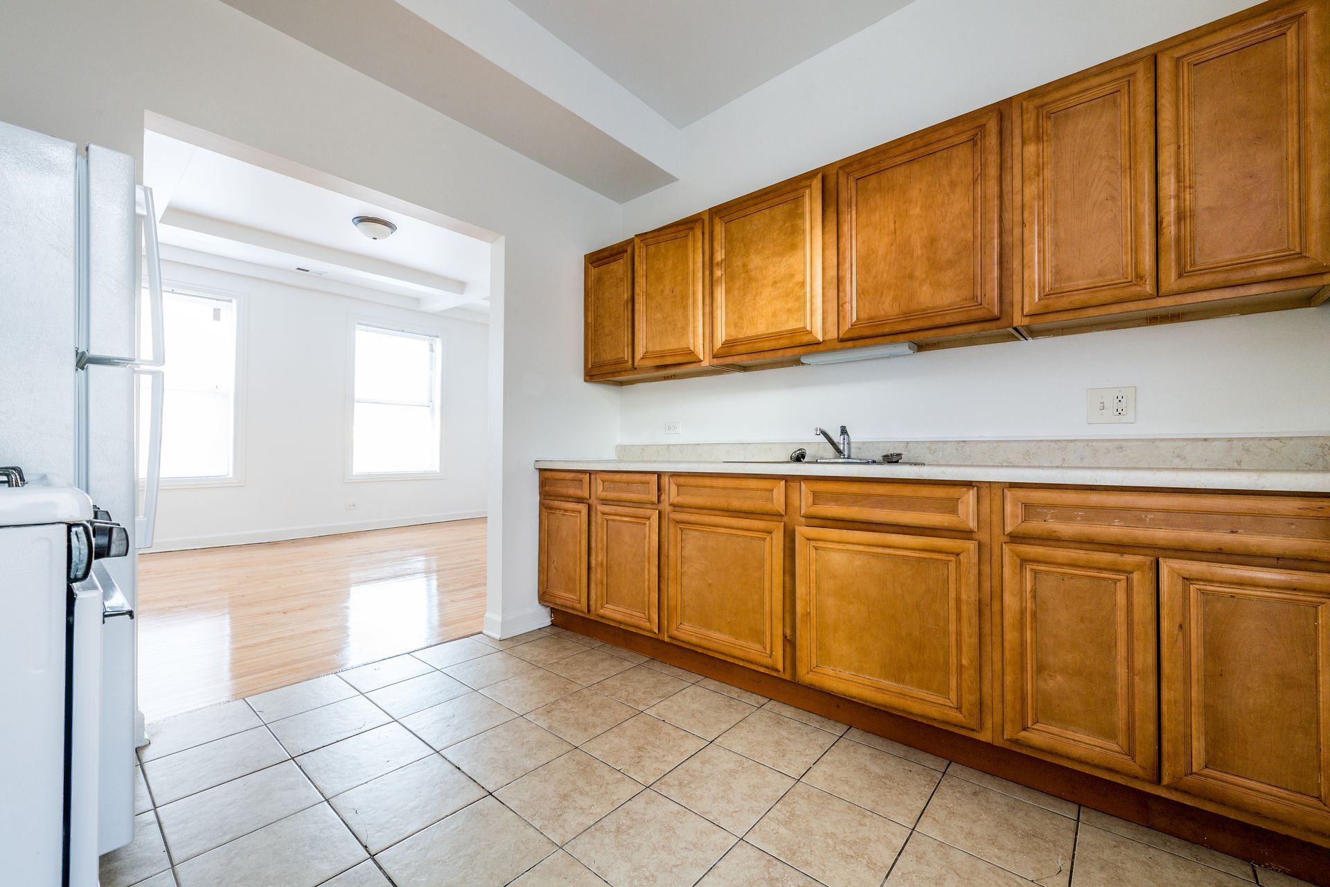 Kitchen with wooden cabinets, light countertops, and tile floor, opening to a room with wood flooring.